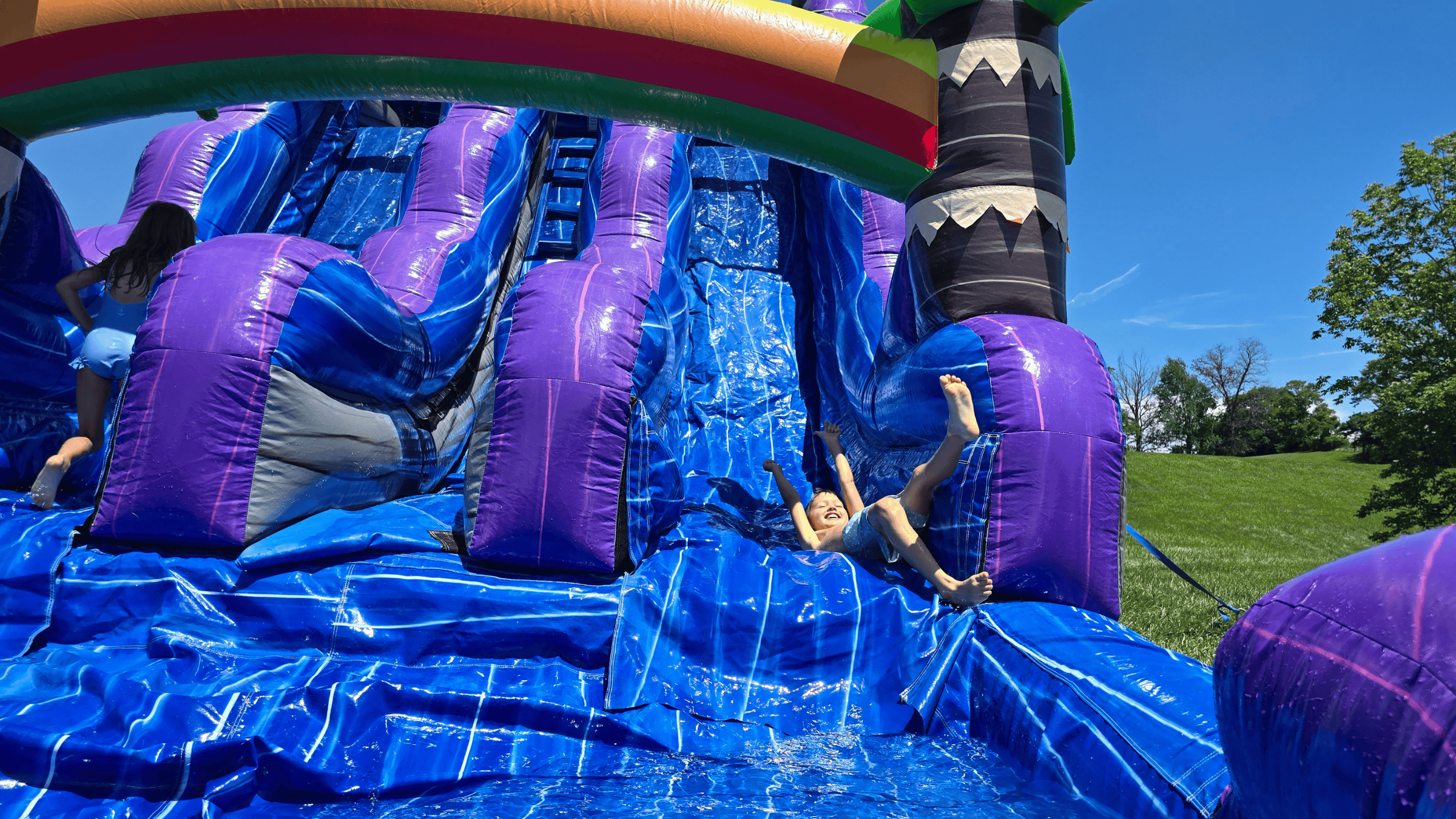 Kid sliding down the Purple Plunge inflatable water slide rental from Backyard Responders
